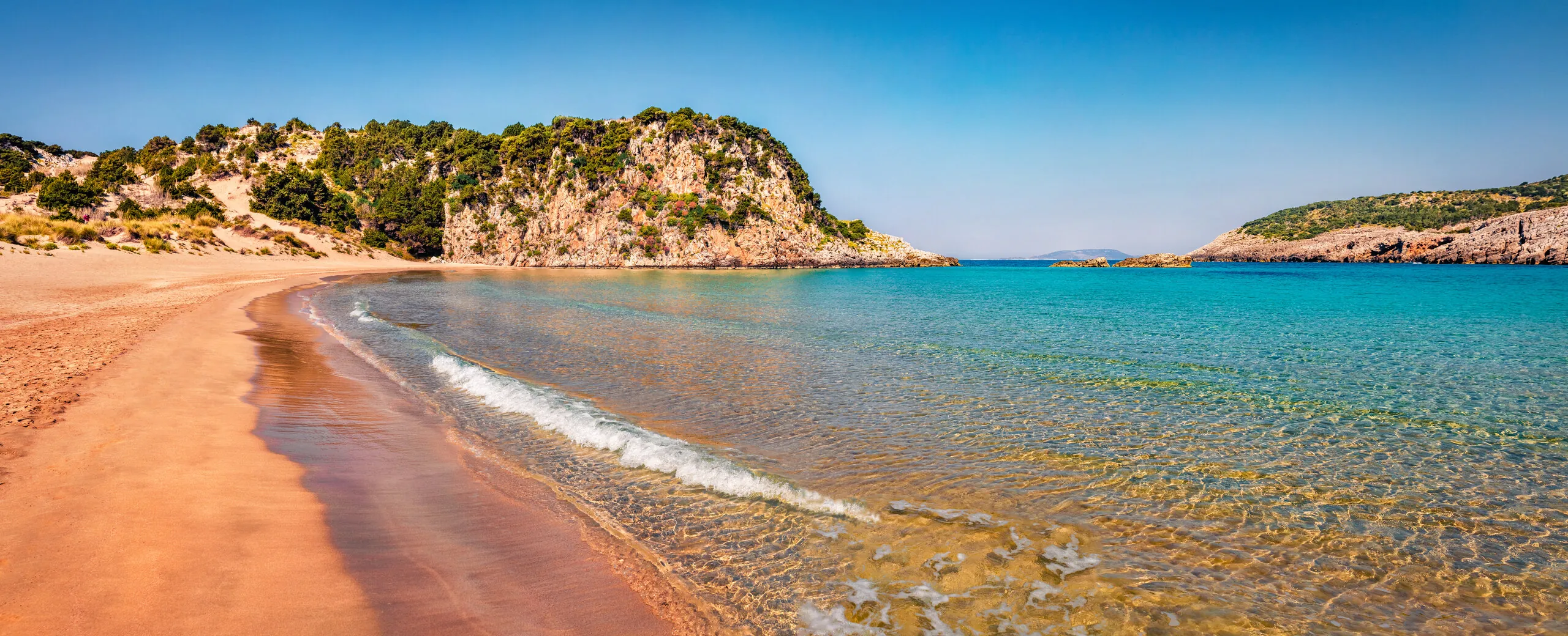 Spiaggia di sabbia dorata e mare turchese sotto un promontorio verde