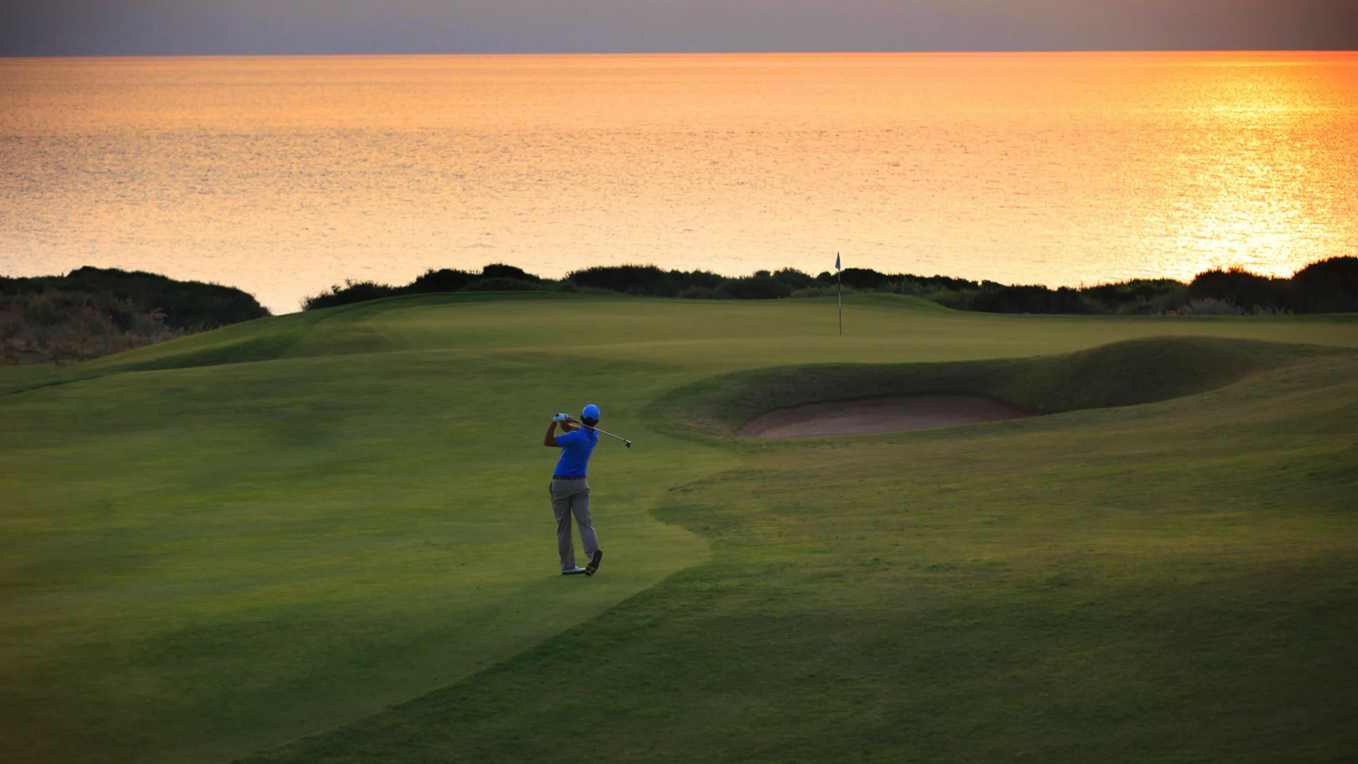 Un golfista sul green al tramonto, con il mare sullo sfondo